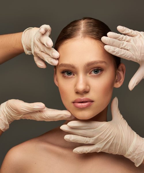 estheticians in medical gloves examining face of young woman on grey background, facial treatment estheticians in medical gloves examining face of young woman on grey background, facial treatment
